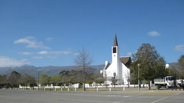 A white church with a slender spire stands beside a broad road.