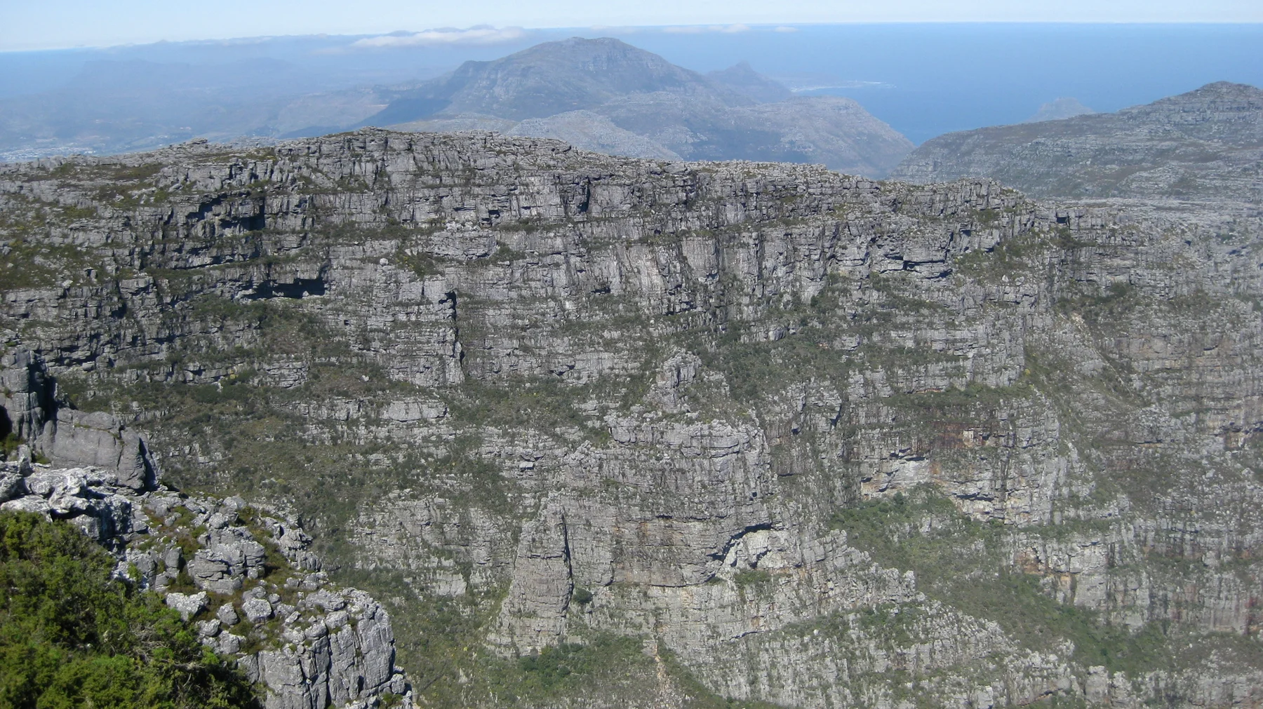 A broad flat-topped cliff reveals horizontal rock layers above a deep drop.