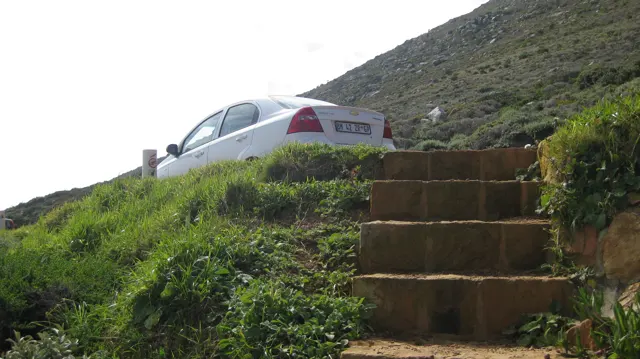 Stone steps climb a grassy bank toward a parked white car.