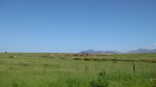 Fenced green grassland stretches toward distant low mountains.
