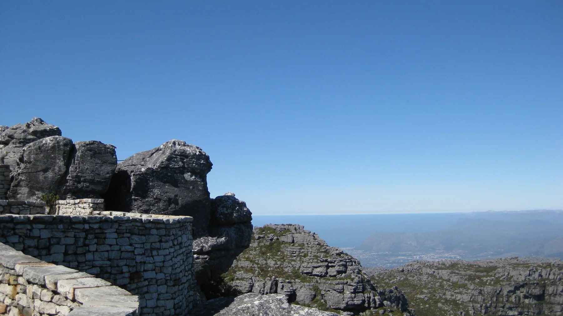 A low stone wall stands among dark boulders beneath clear blue sky.