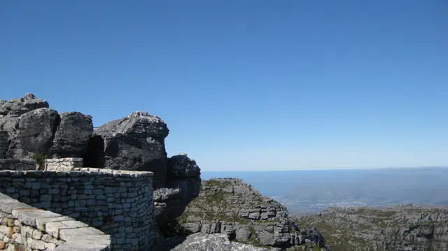 A low stone wall stands among dark boulders beneath clear blue sky.