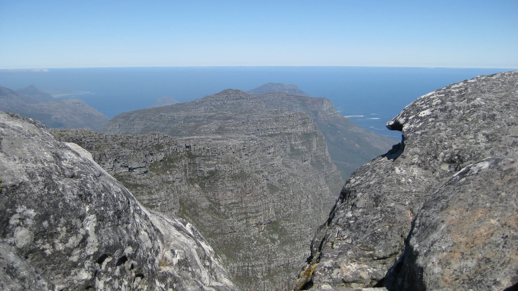 Large boulders frame a sheer cliff and distant sea.