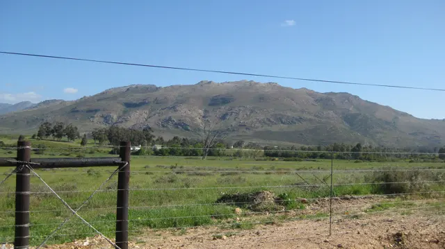 A broad mountain rises beyond a gate and green fenced land.