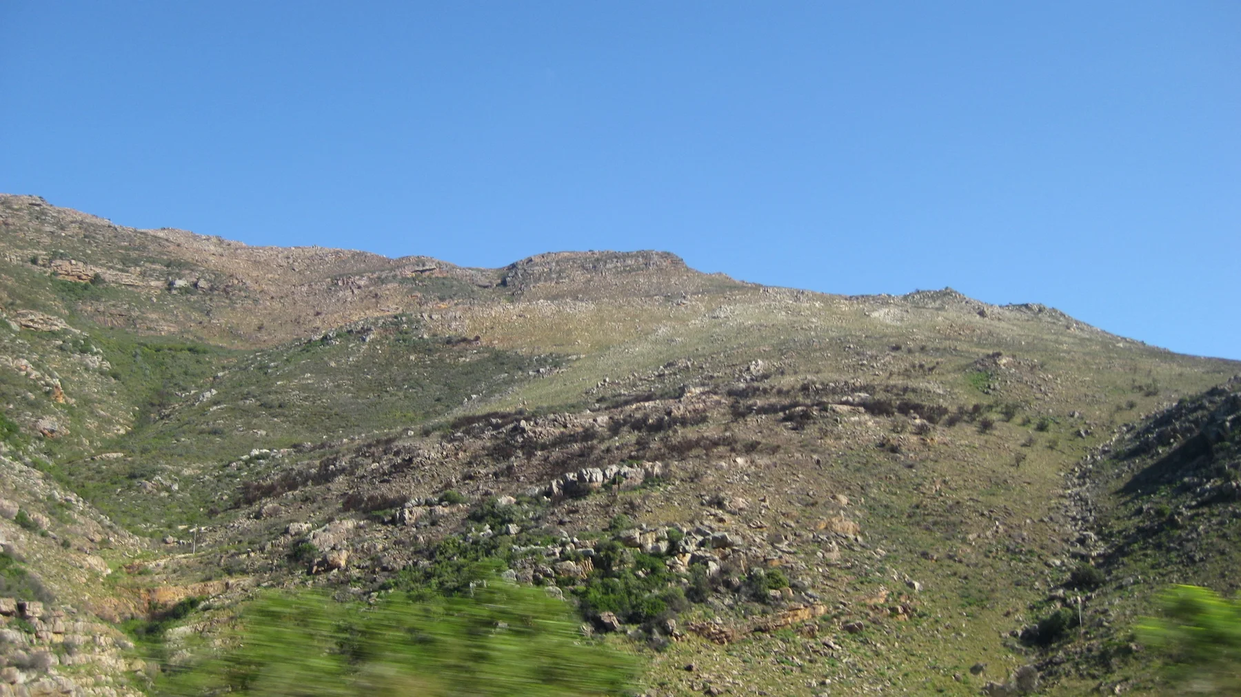 Bands of exposed rock cross a sparsely green hillside.
