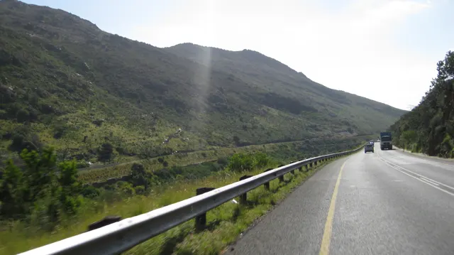 A road and metal guardrail follow the base of a steep green mountain.