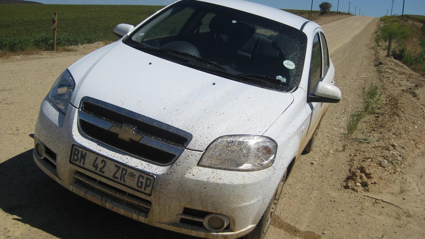A white car stands at an angle on a dusty rural road.