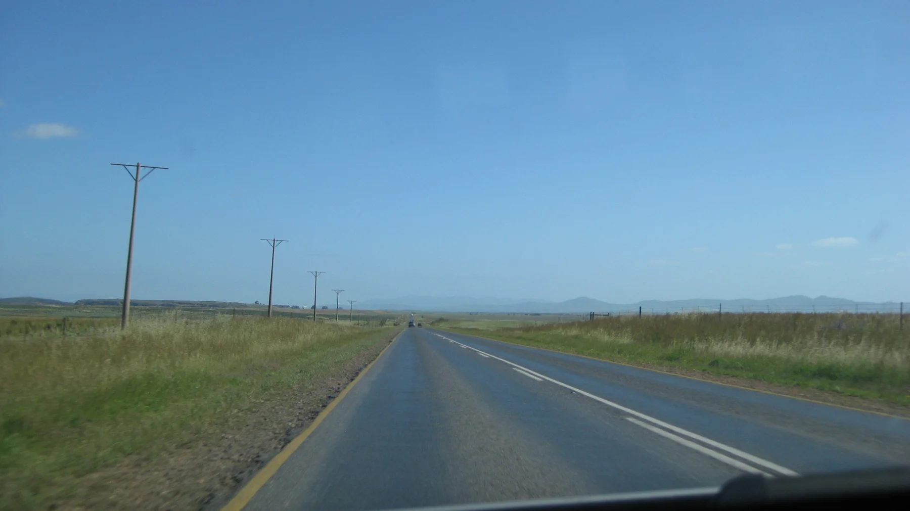A straight paved road follows utility poles across flat fields.