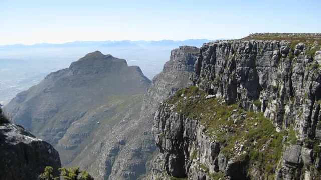 A pointed mountain rises beyond a high layered cliff.