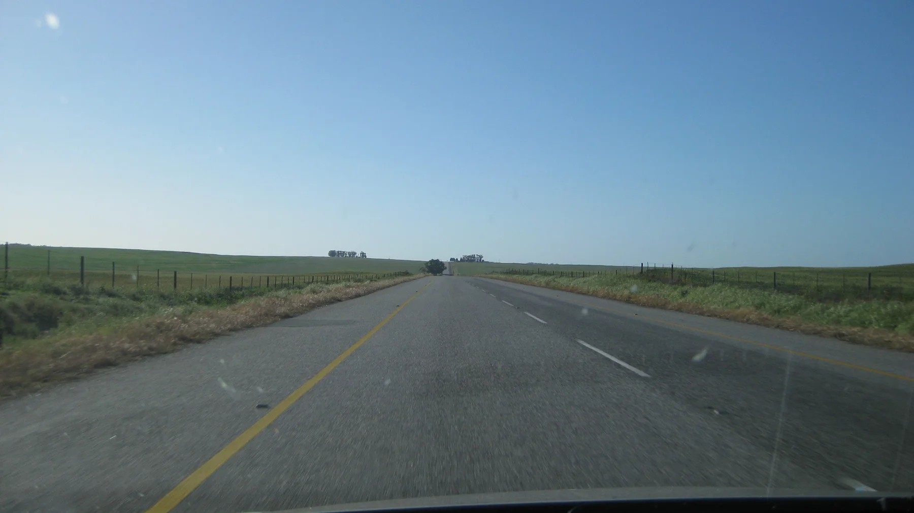 A straight road crosses flat fields under cloudless blue sky.