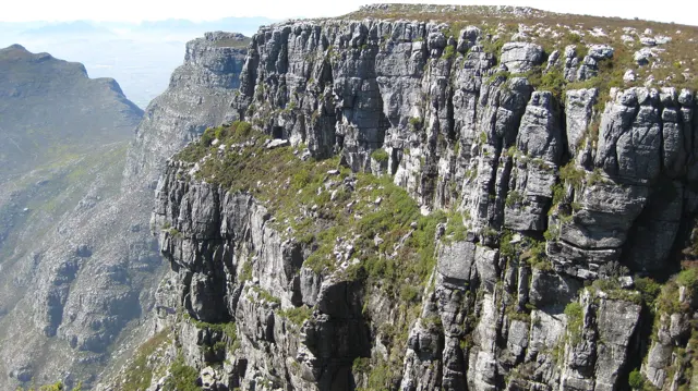 A steep cracked cliff drops below a flat green summit.