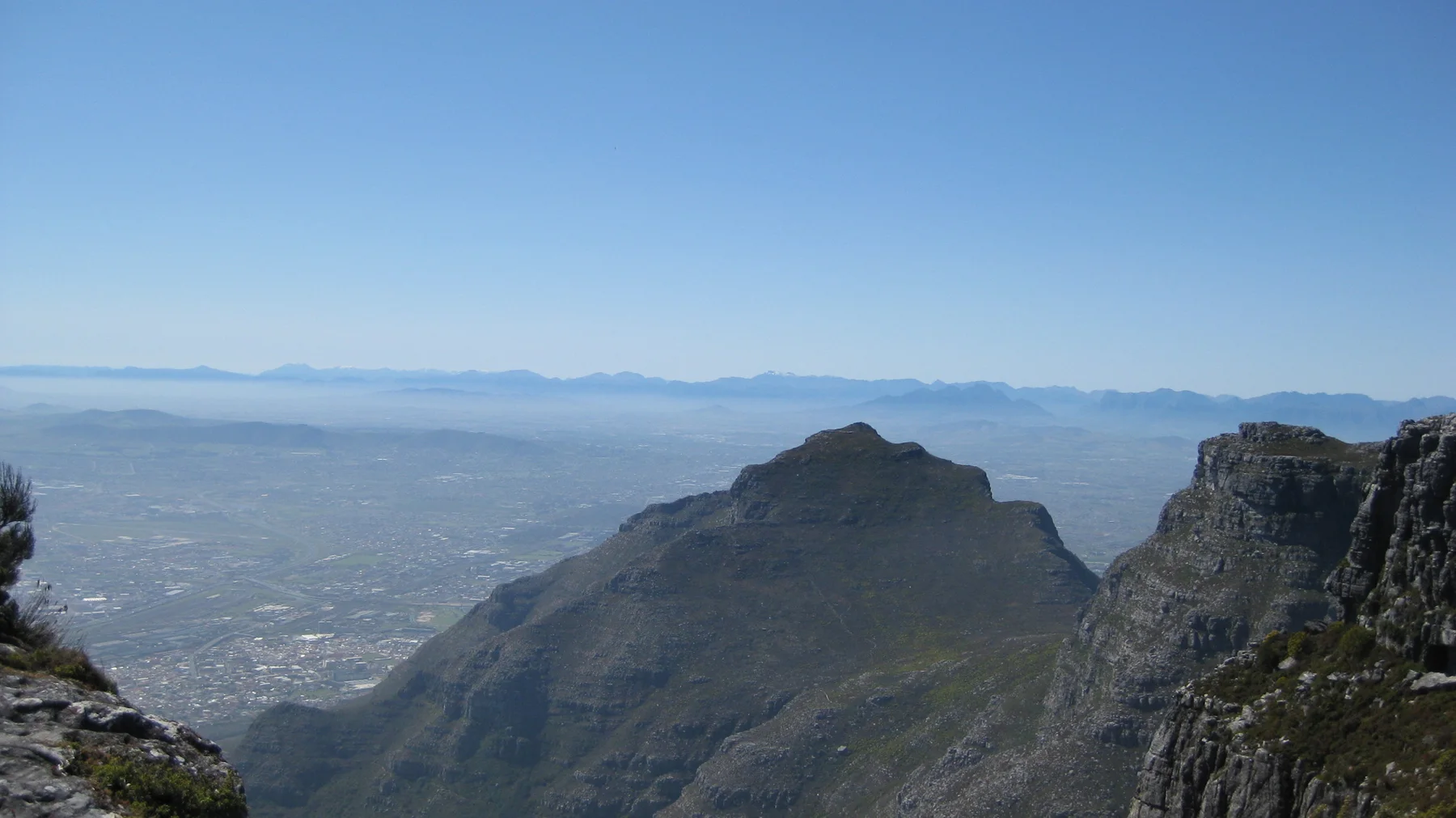 A dark peak rises above a hazy developed valley.