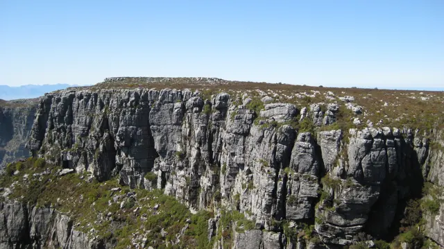 A flat plateau ends in a steep dark rock wall.