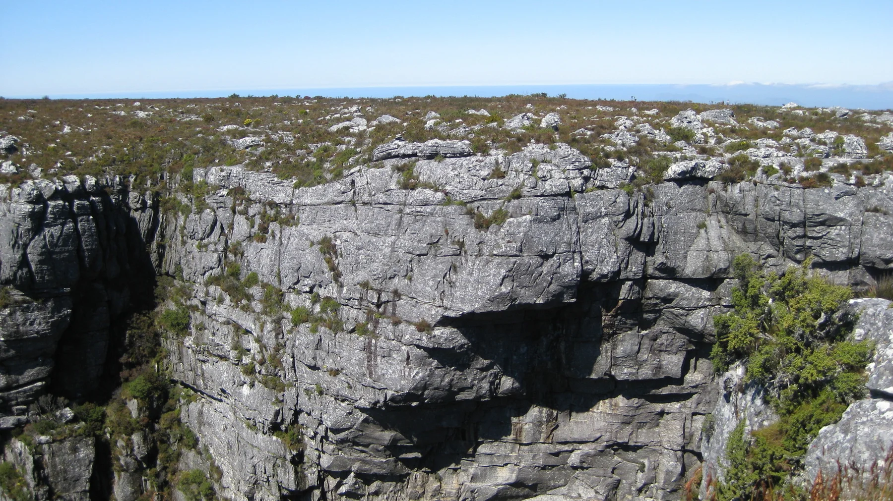 A deep shadow marks a broken section of cliff below the plateau.