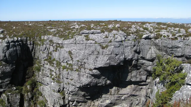 A deep shadow marks a broken section of cliff below the plateau.