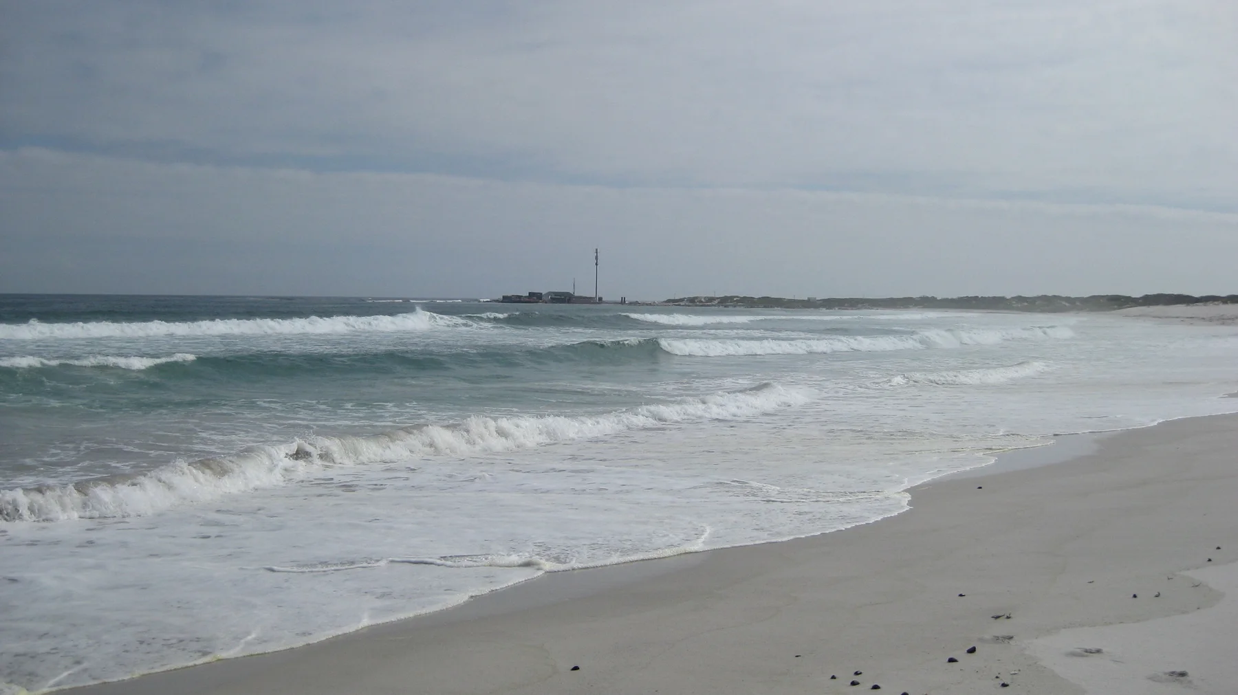 Gray-green waves wash across a pale sandy beach.