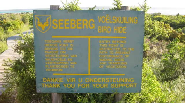 A sign marks Seeberg Bird Hide beside low coastal vegetation.