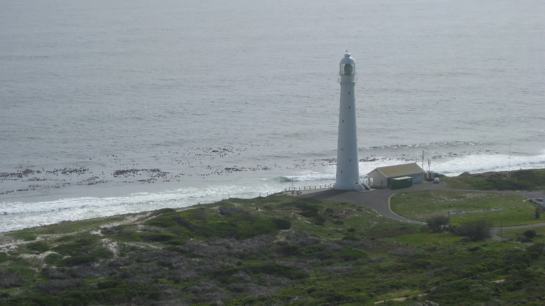 A tall pale lighthouse stands beside a narrow beach and gray sea.