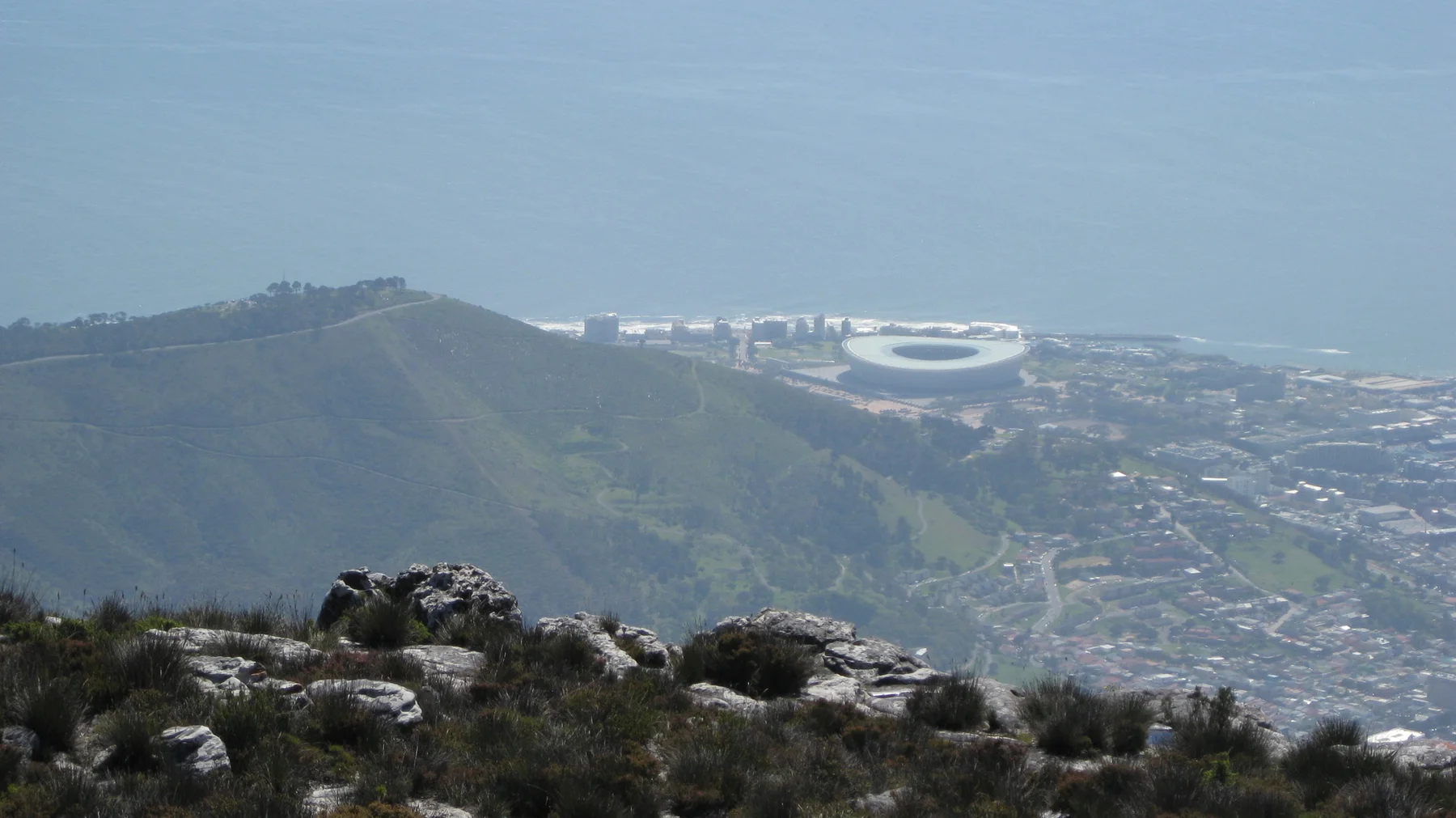 A pale oval stadium appears beyond a dark hill and city buildings.