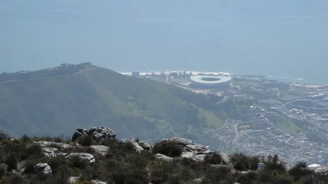 A pale oval stadium appears beyond a dark hill and city buildings.