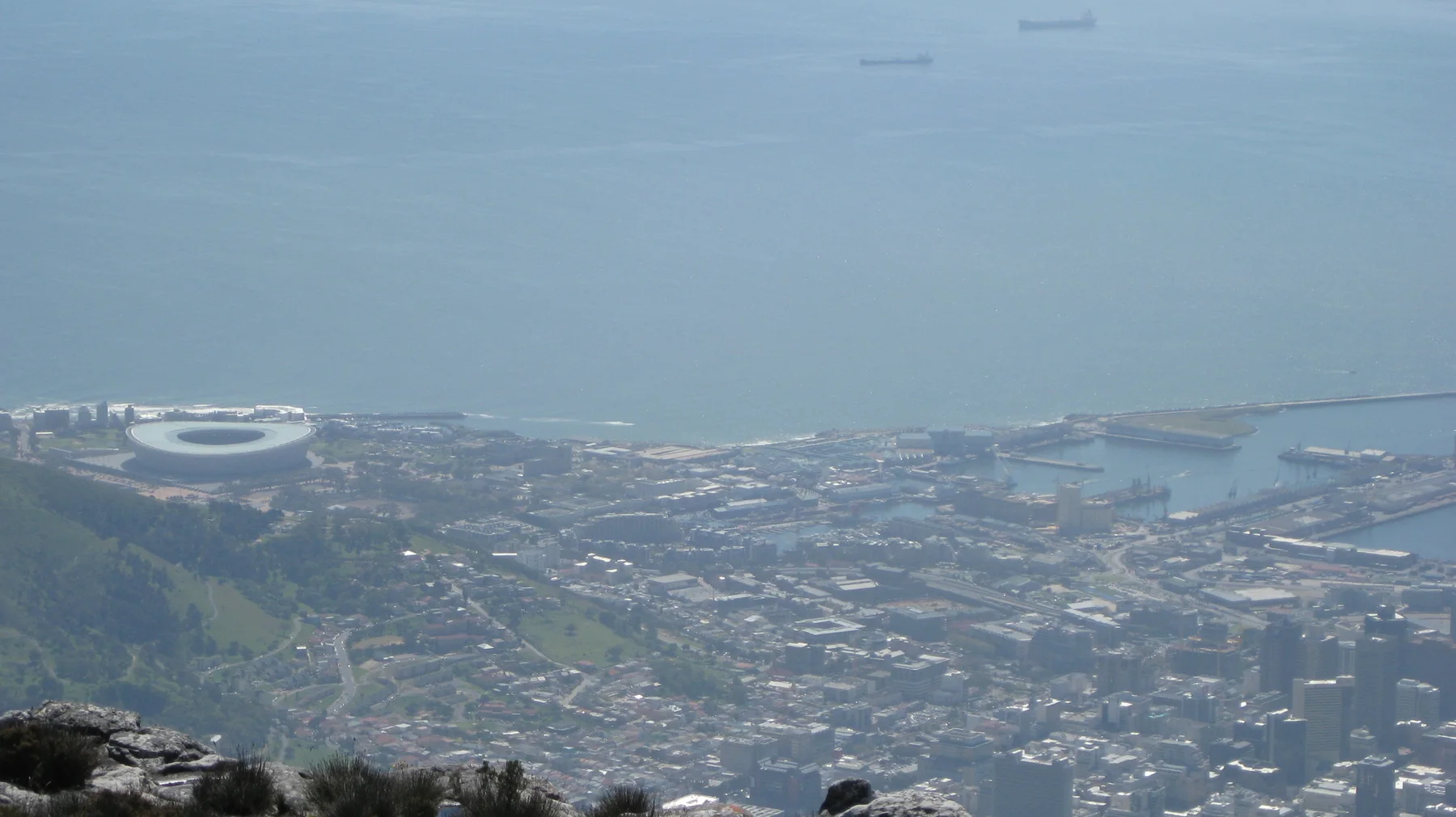 City buildings and harbor water fade into haze beyond summit rocks.