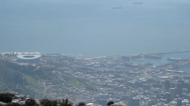 City buildings and harbor water fade into haze beyond summit rocks.