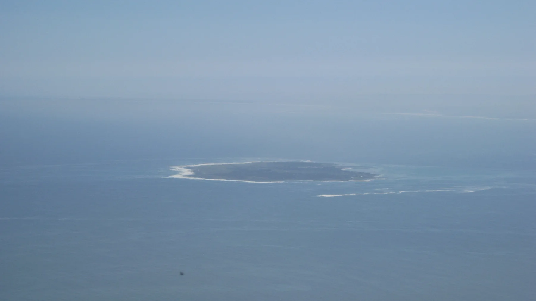 A low offshore island appears through blue-gray ocean haze.