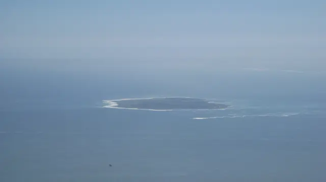 A low offshore island appears through blue-gray ocean haze.