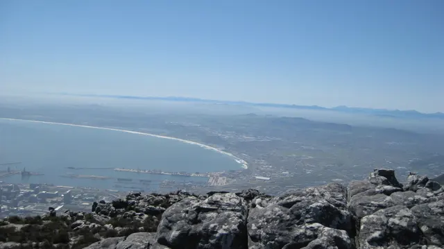 A sweeping bay curves beyond summit rocks and a hazy city.