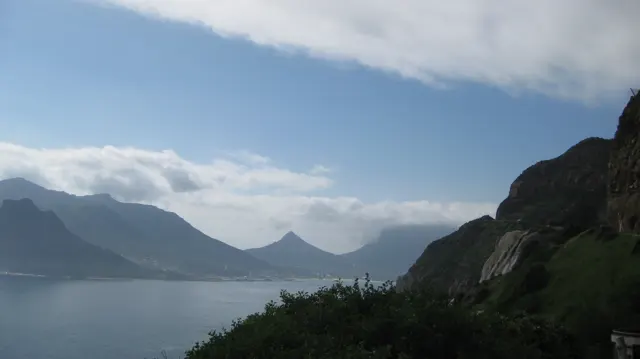 Calm water lies between steep mountain slopes beneath white clouds.