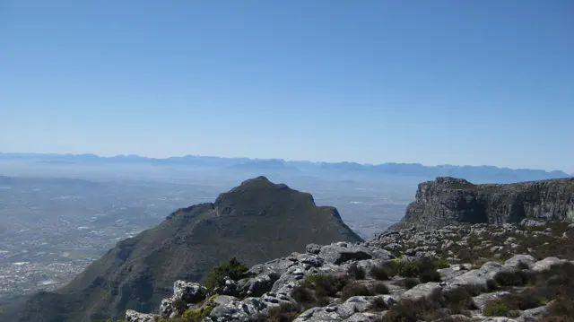 A prominent peak rises beyond low rocks and scrub on a plateau.