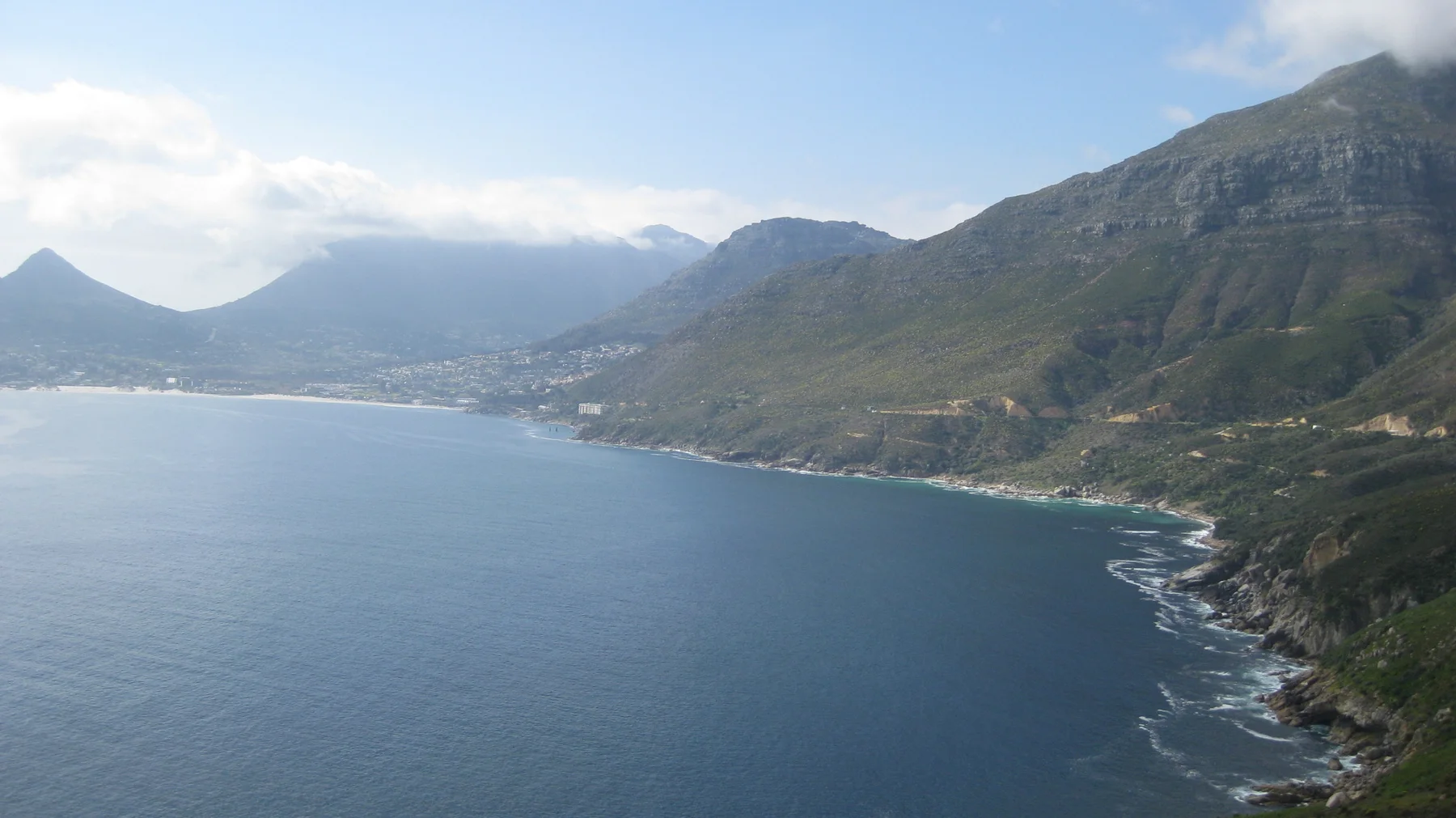 A steep mountain shoreline follows the edge of calm blue water.