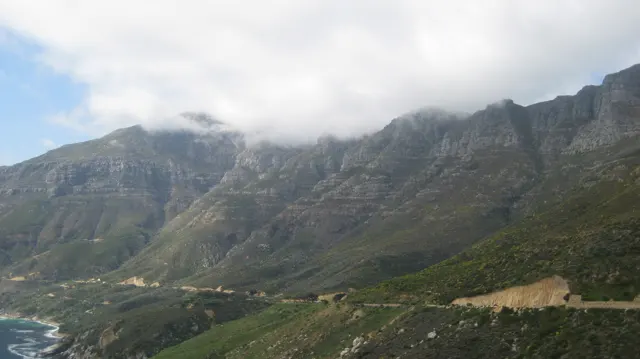 Clouds drift over a steep mountain wall above the coast.