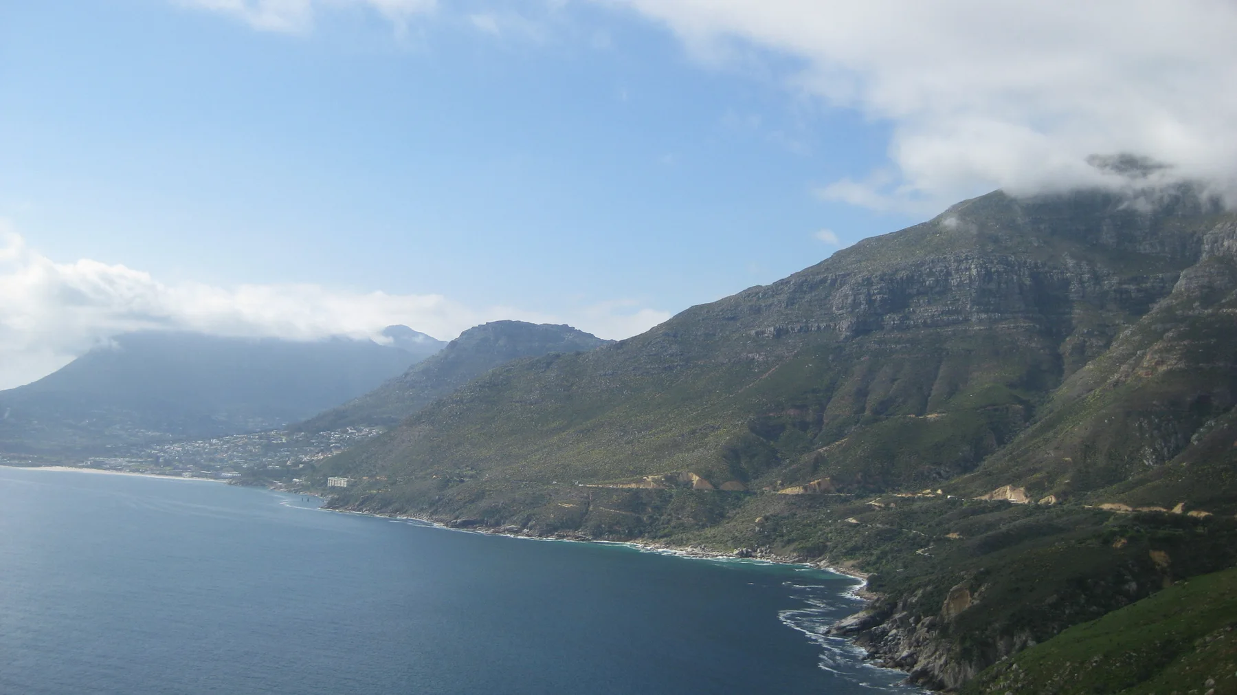 Calm bay water borders a steep ridge with cloud near its top.