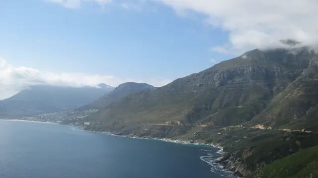 Calm bay water borders a steep ridge with cloud near its top.