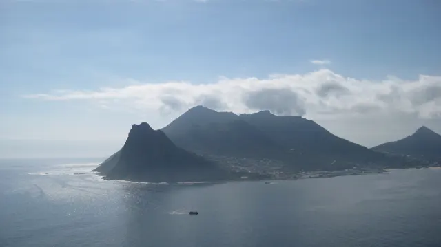 A small boat sits below a dark mountain headland across the bay.