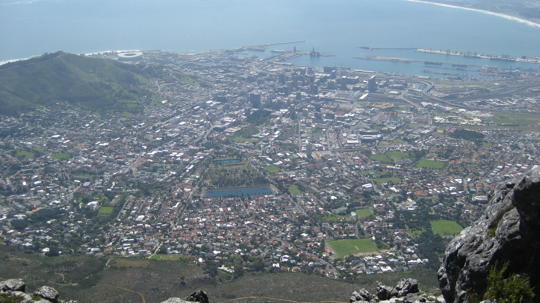 Dense buildings spread toward harbor water below a rocky viewpoint.