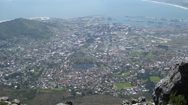 Dense buildings spread toward harbor water below a rocky viewpoint.