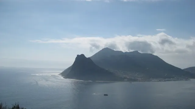 Still blue water lies beneath a dark mountain and a white cloud band.