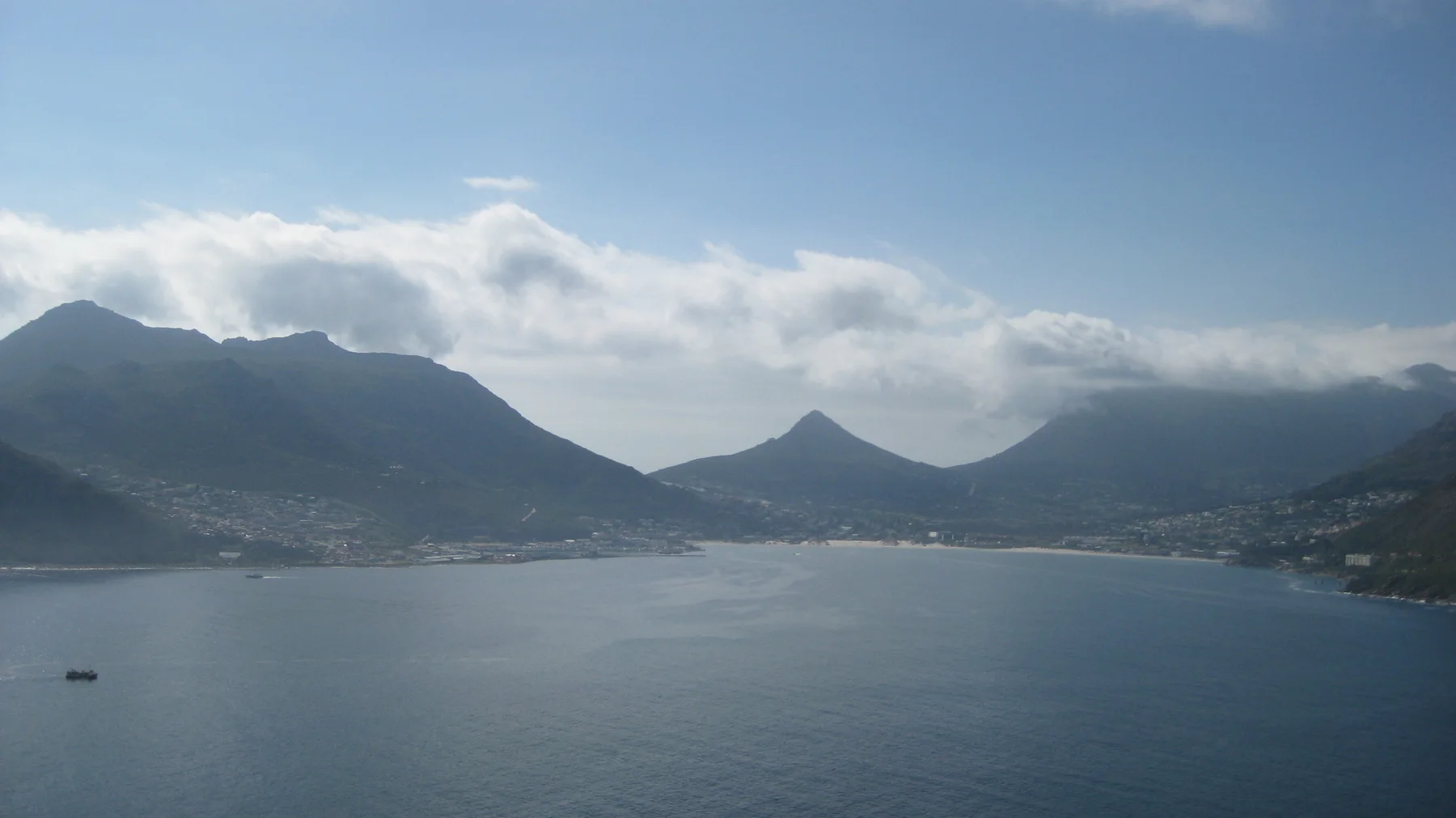 A calm bay lies below several peaks under a strip of cloud.