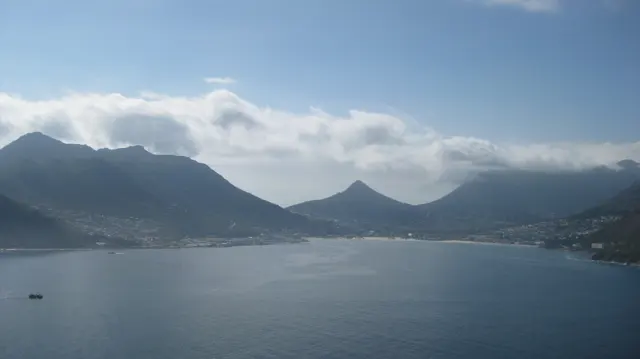 A calm bay lies below several peaks under a strip of cloud.