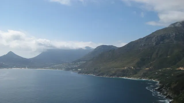A mountain coast curves around deep blue water beneath low clouds.