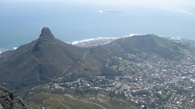 A sharply pointed hill rises above city buildings beside the ocean.