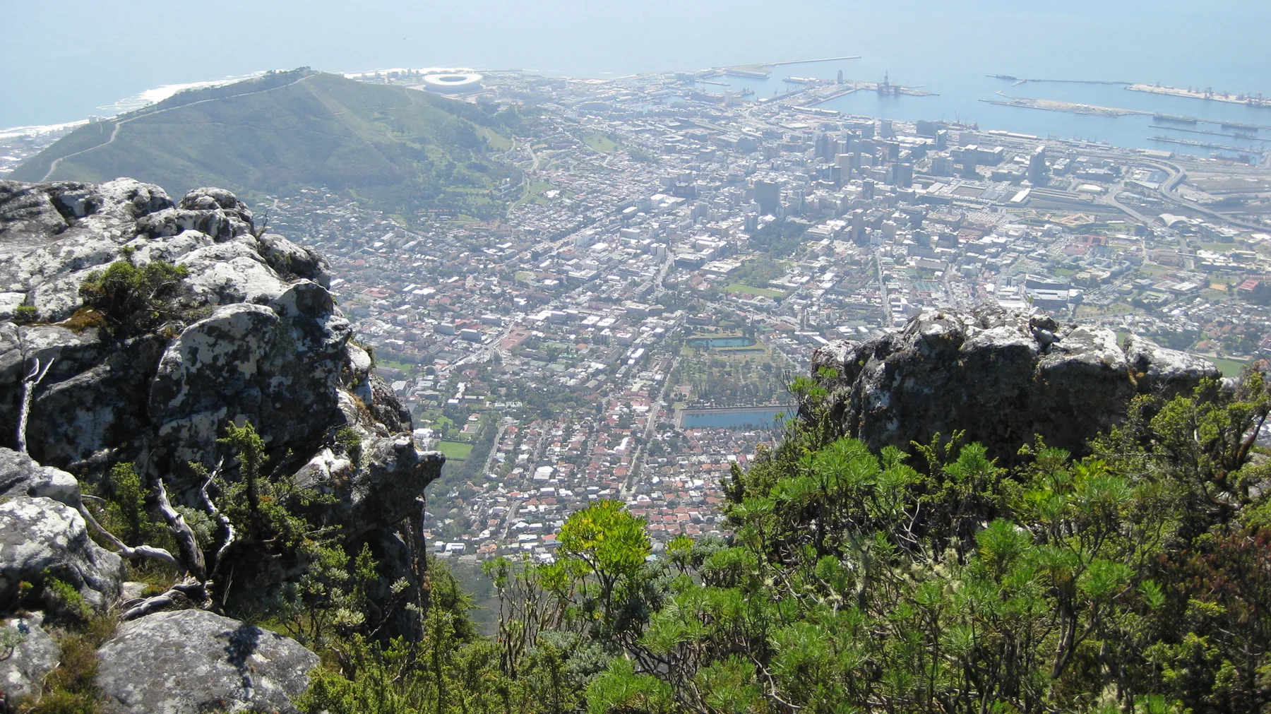 A gap between summit rocks reveals dense city buildings far below.
