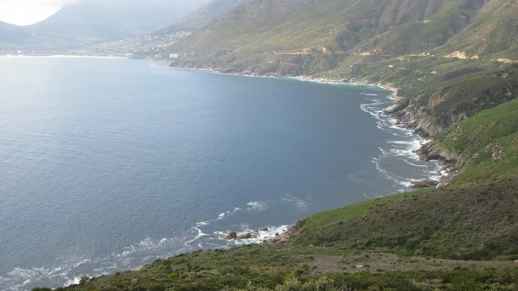 A quiet blue bay curves below steep green coastal slopes.