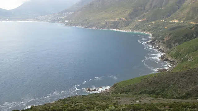 A quiet blue bay curves below steep green coastal slopes.
