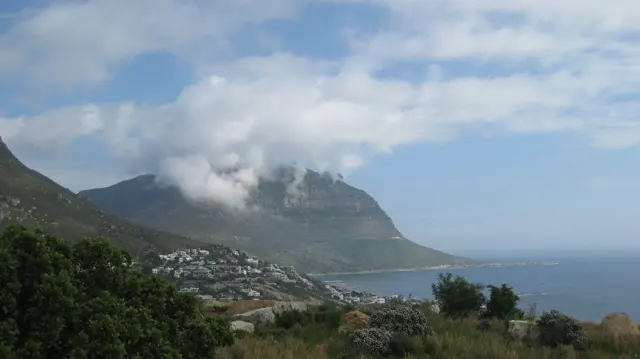 Low cloud wraps a mountain above coastal houses and blue water.