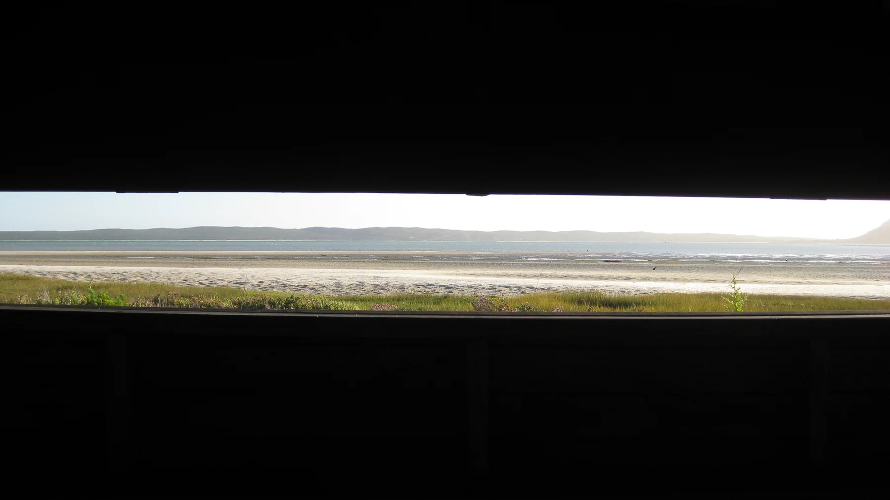 A horizontal hide opening frames a strip of shore and water.