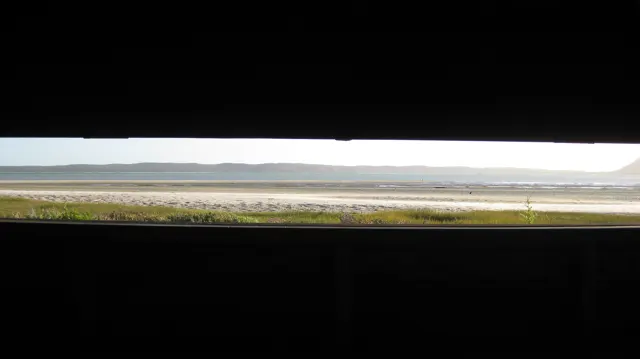 A horizontal hide opening frames a strip of shore and water.