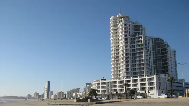 A tall stepped apartment building overlooks the beach beneath blue sky.